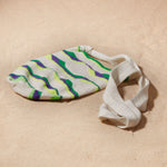 Flat view of ivory, green, neon green, purple woven bag on a sand background