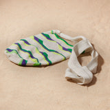 Flat view of ivory, green, neon green, purple woven bag on a sand background