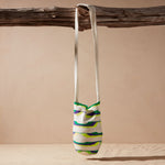 Ivory, green, neon green, purple woven bag hanging by its strap on a branch against a beige background