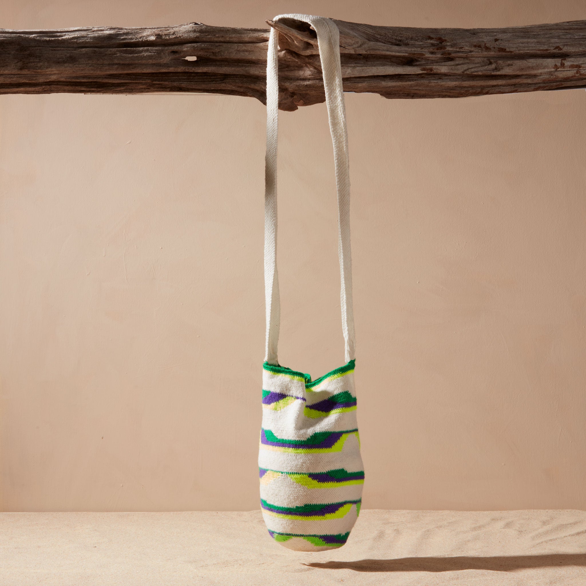 Ivory, green, neon green, purple woven bag hanging by its strap on a branch against a beige background