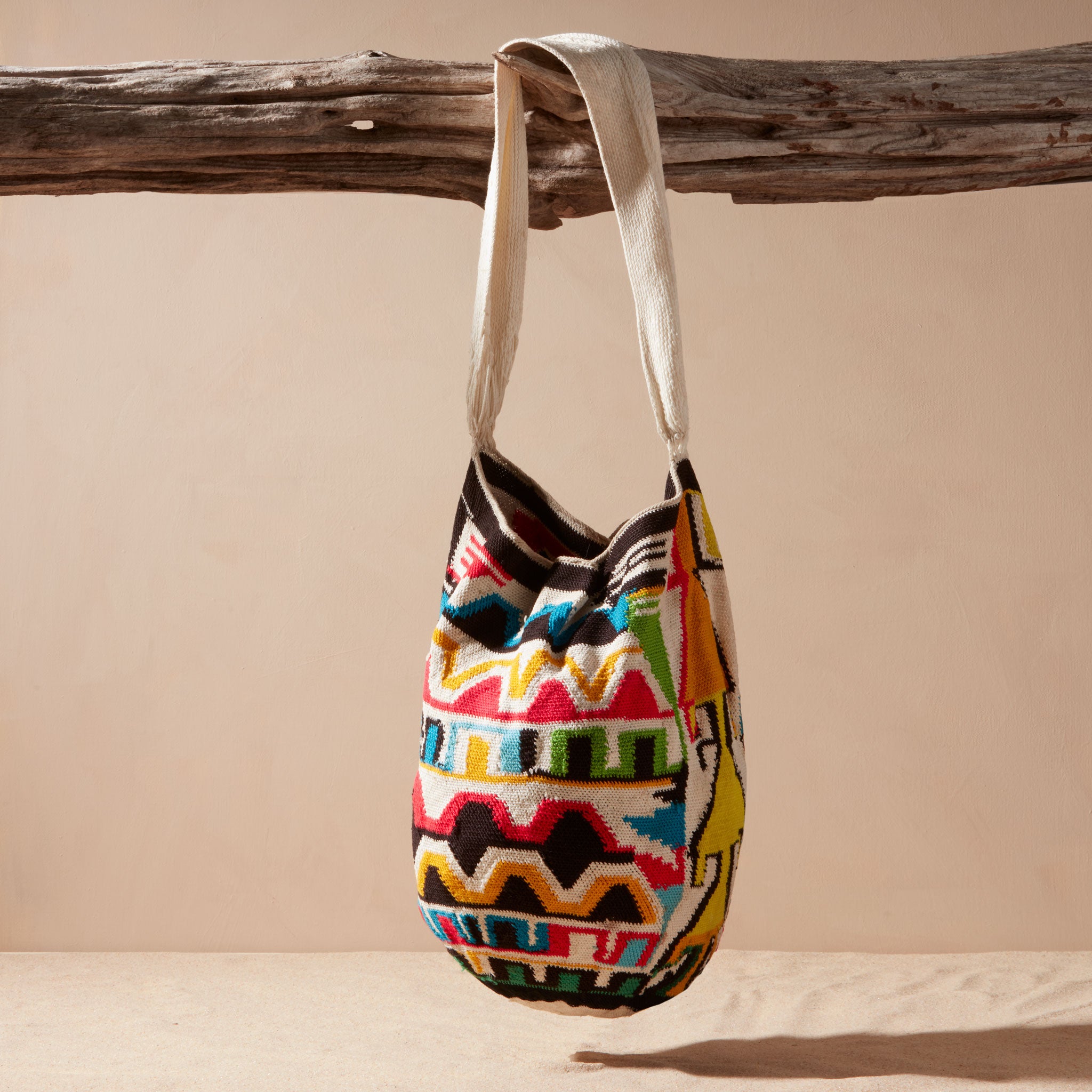Colorful patterned bag hanging on a wooden branch against a beige background