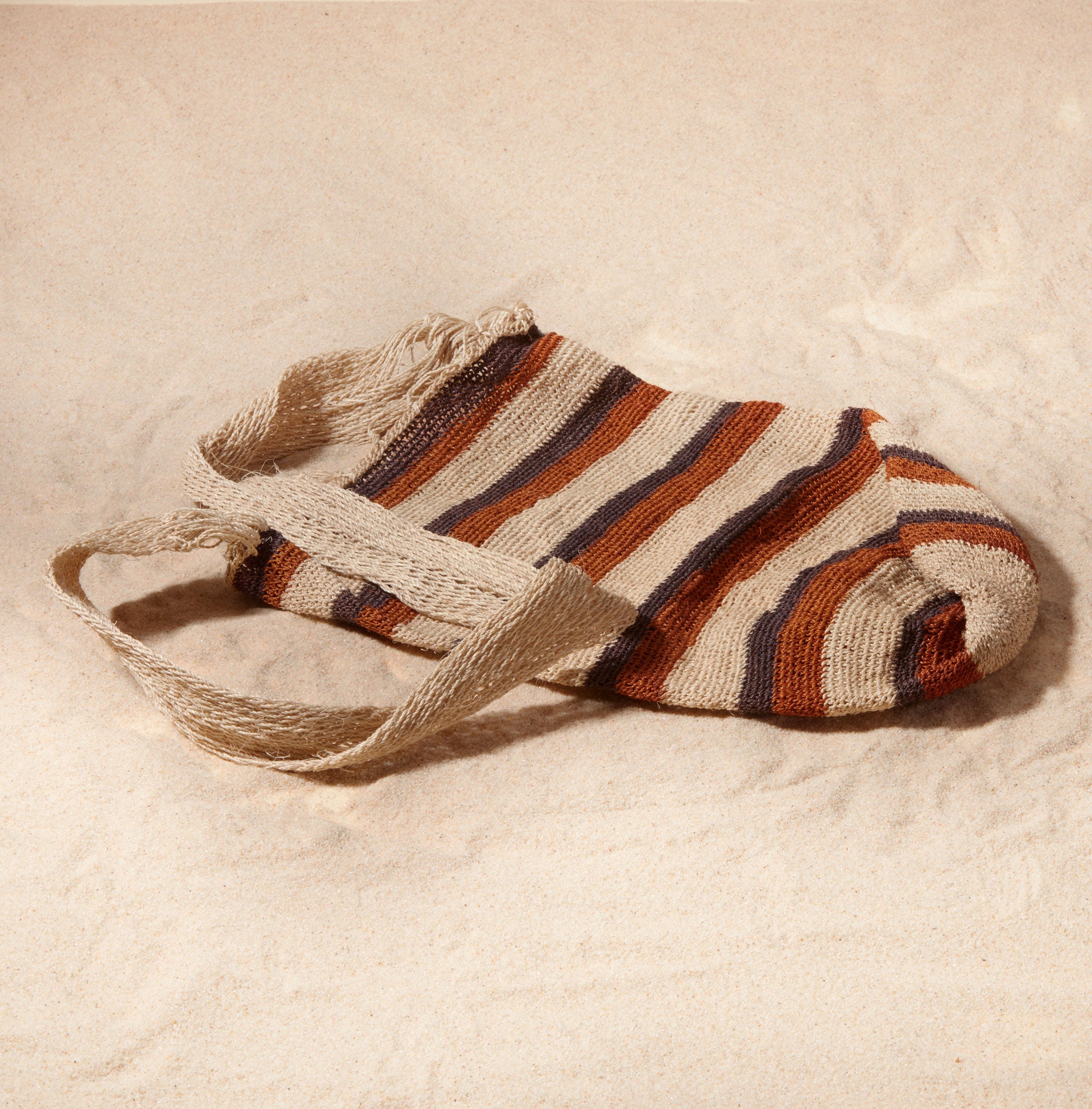 Flat view of striped woven bag against a sand background