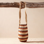 Striped woven bag hanging on a wooden branch against a beige background