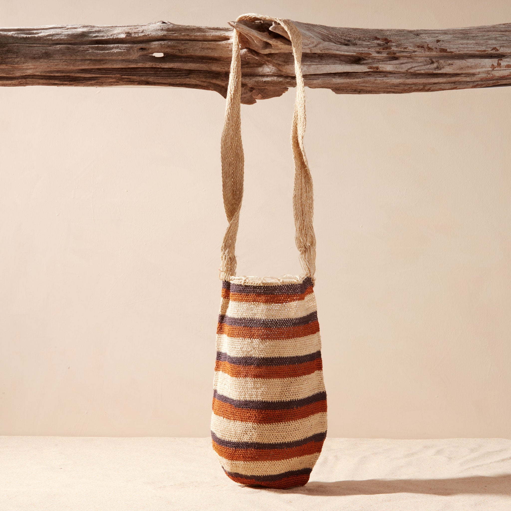 Striped woven bag hanging on a wooden branch against a beige background