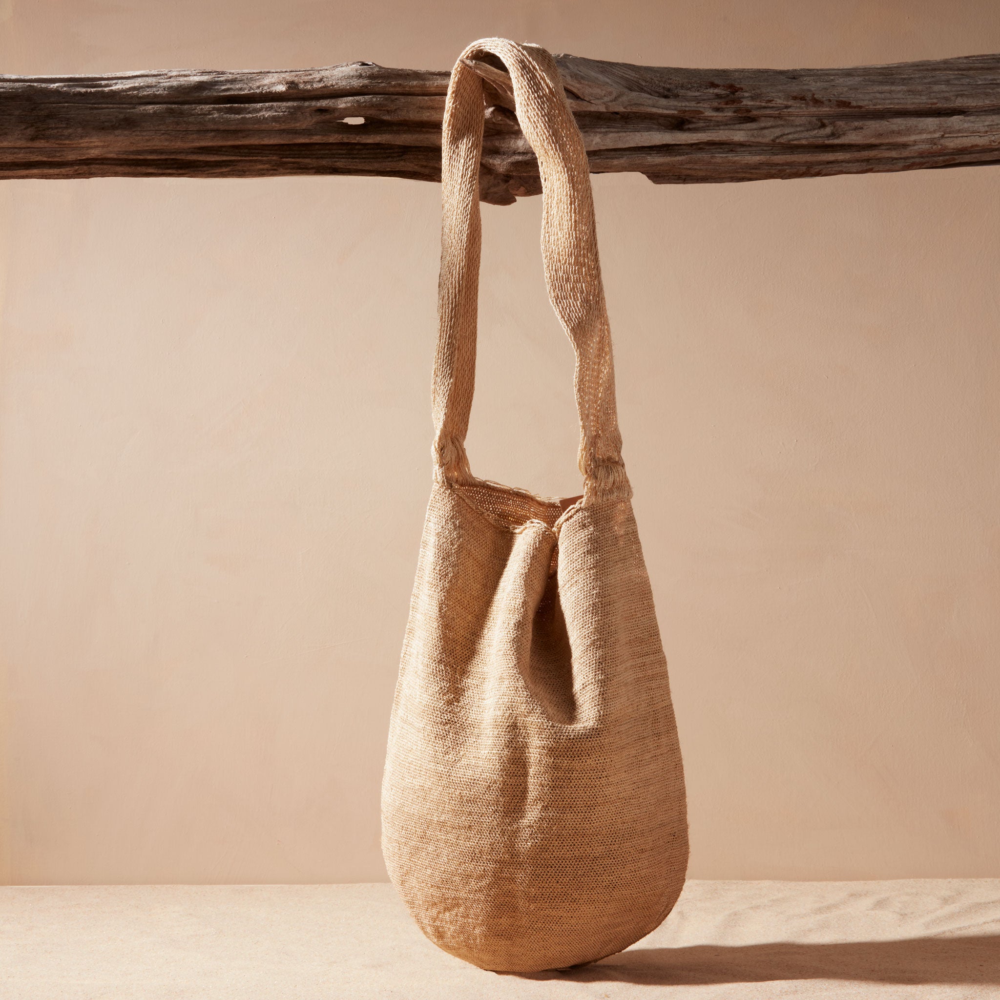 Beige woven handbag hanging on a wooden branch against a beige background
