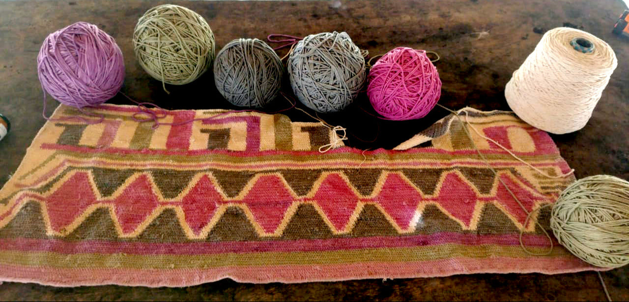 Yarn balls and a spool of cotton used to make the geometric pattern fabric below on a wooden table.