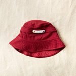 Flat view of red bucket hat with a white and colorful beaded patch on a sand background