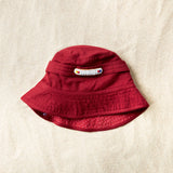 Flat view of red bucket hat with a white and colorful beaded patch on a sand background