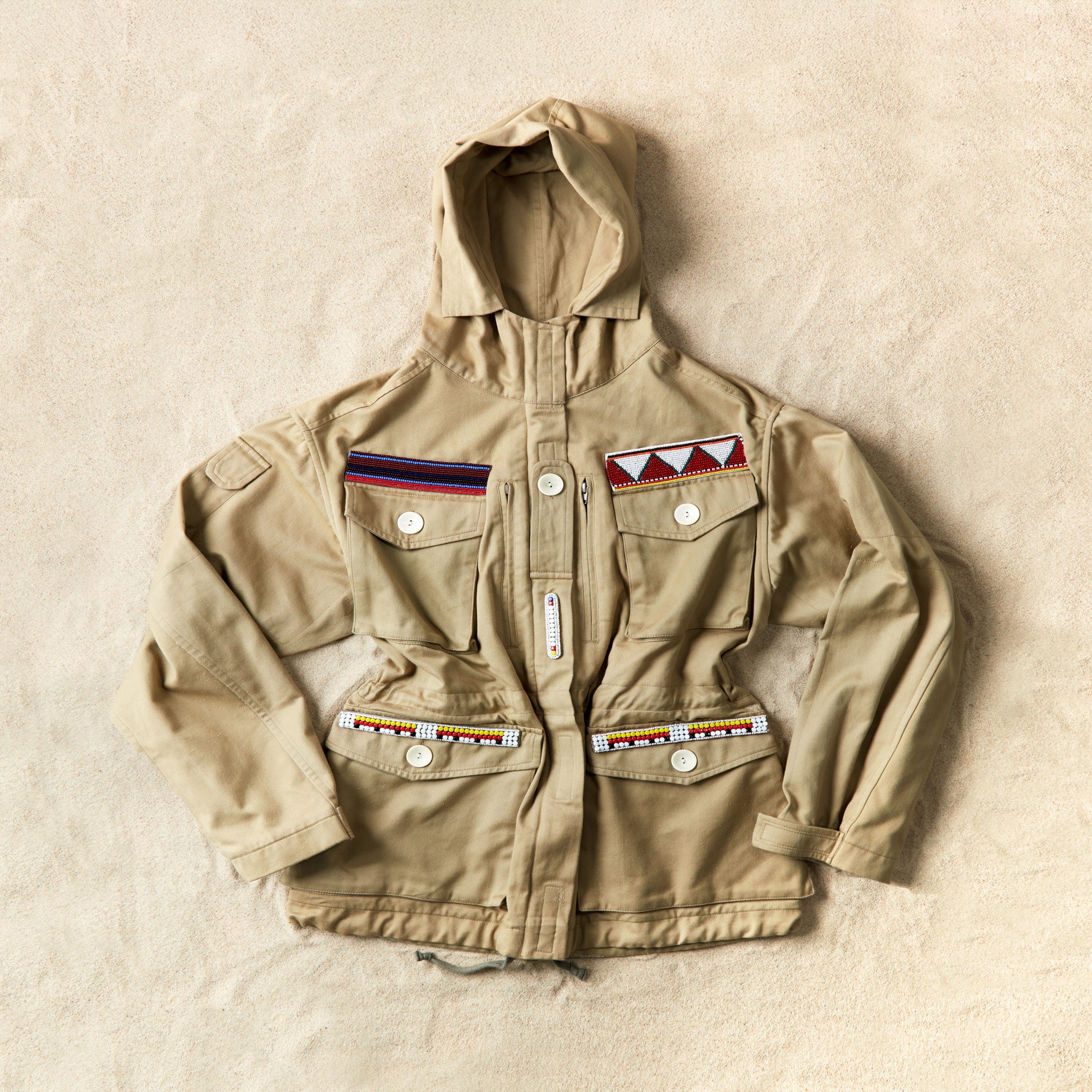 Khaki ranger safari hooded jacket with colorful hand beaded patches against a sand background