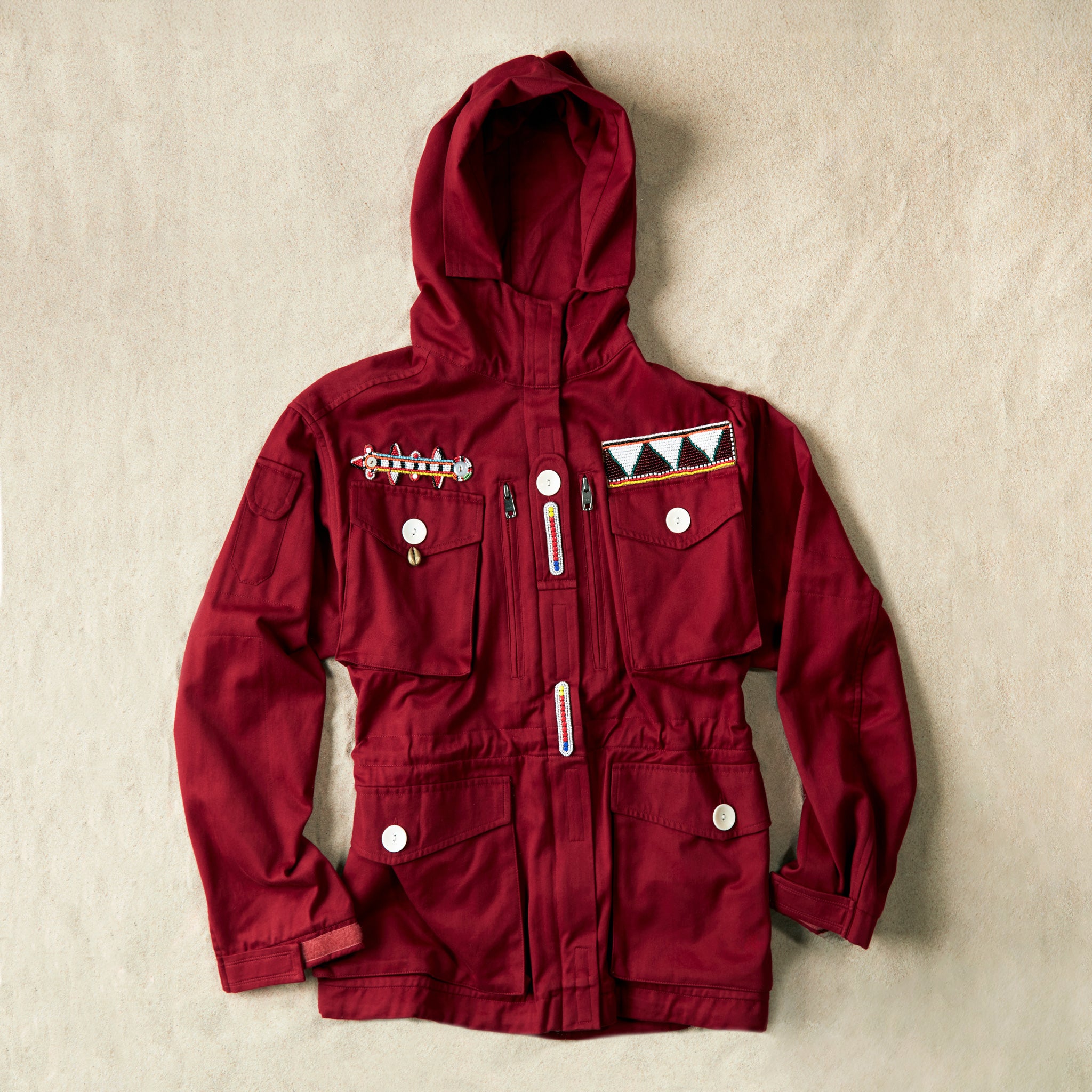 Red ranger hooded safari jacket with colorful hand beaded patches on a sand background