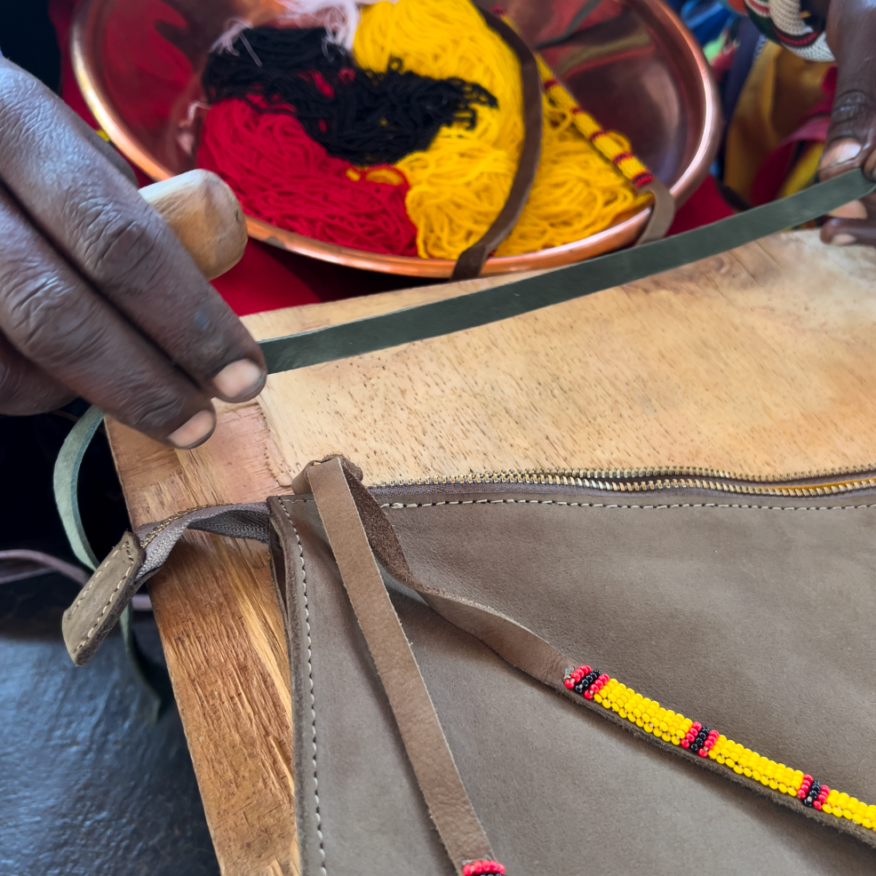 Person working on a suede leather pouch with colorful beads in a metal bowl in the background.