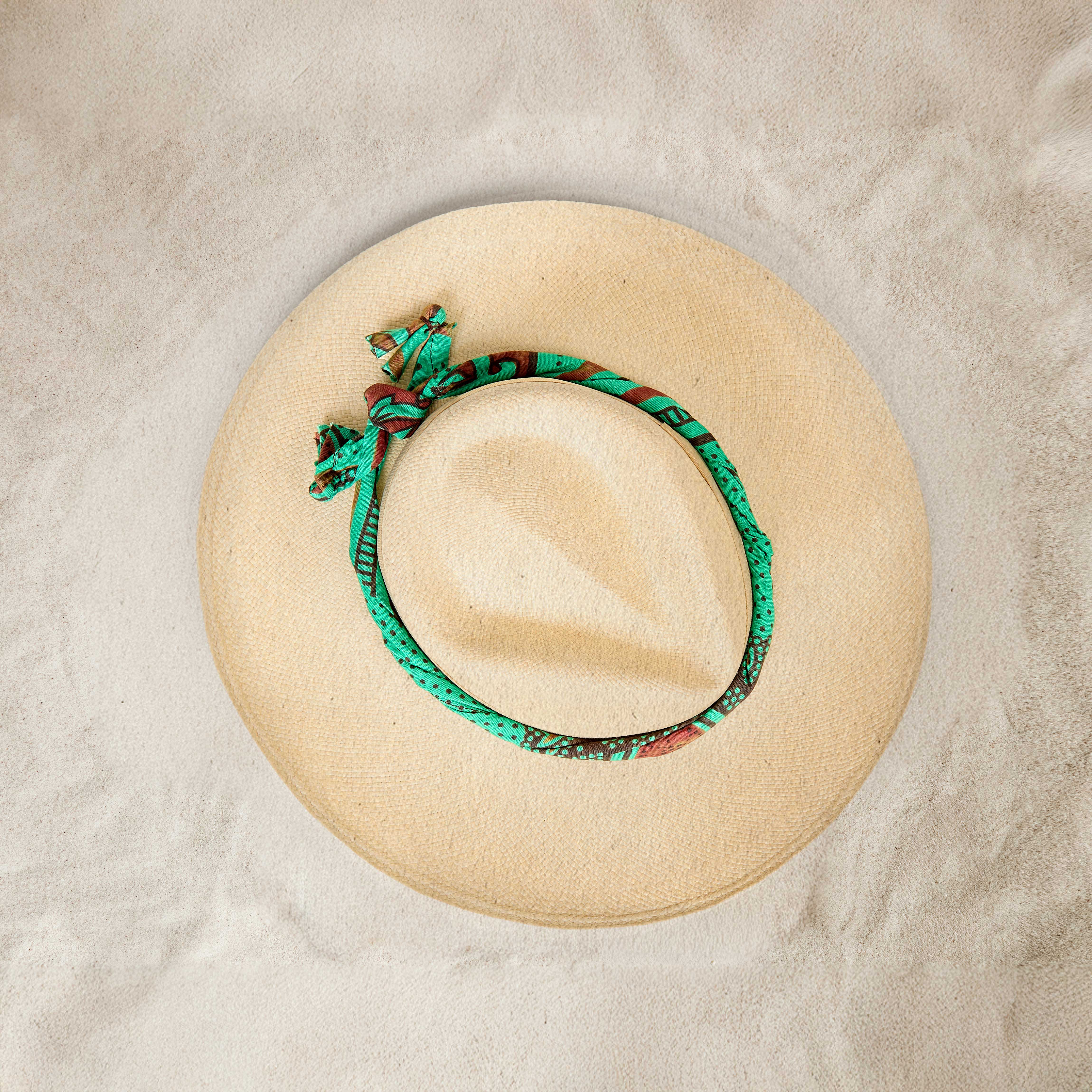Bird's Eye View of matural Straw Hat with Wide Brim with Colorful Green Wrapped Band on Sand Background