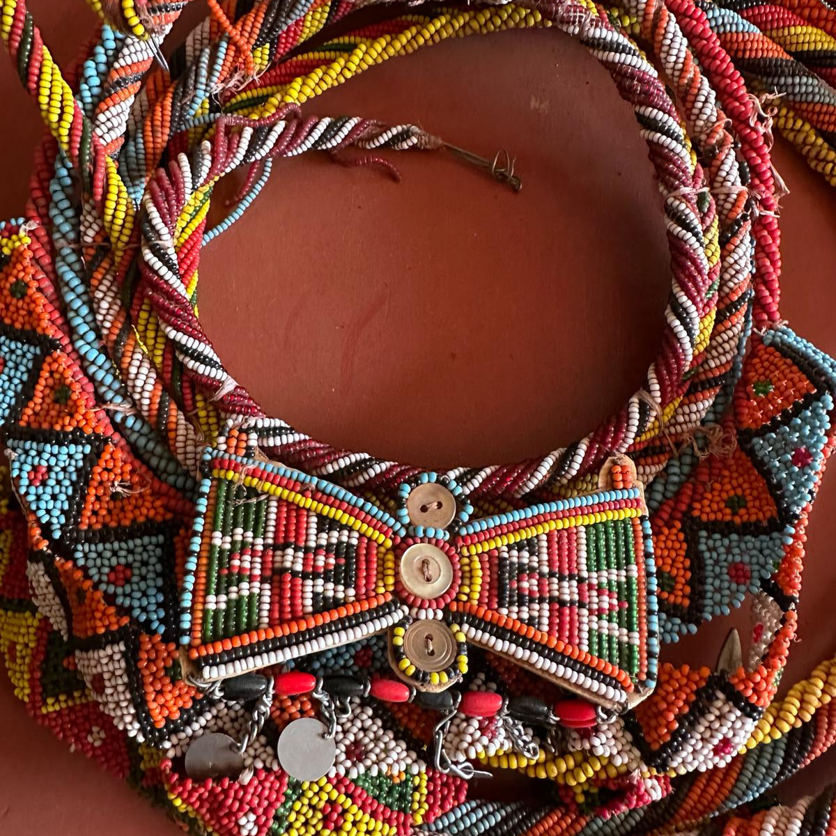 Stack of colorful beaded necklaces against an earth red background