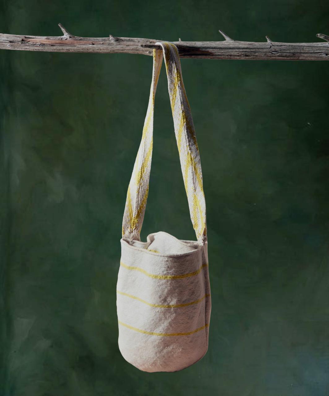 Textile bag with yellow stripes hanging from a branch against a green background